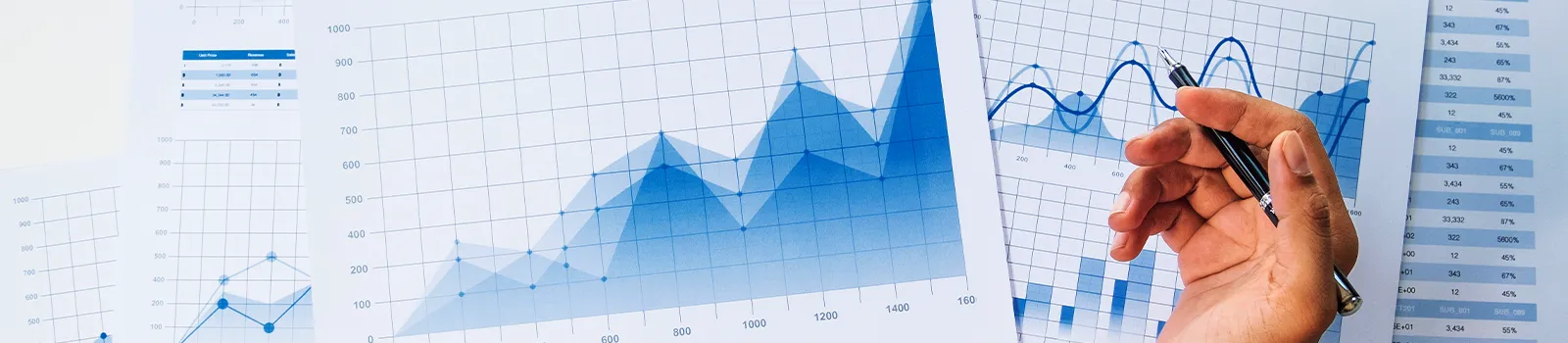 Pages of graphs, tables and charts with a hand atop them holding a pen